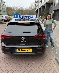 Geslaagde leerling bij de zwarte VW Golf met het 5 Sterren-daklichtbord