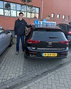 Geslaagde leerling juicht naast de lesauto in Amsterdam