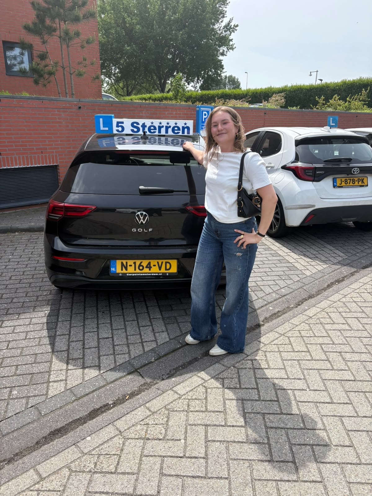 Leerling van Rijschool 5 Sterren naast de zwarte VW Golf met het 5 Sterren-daklichtbord